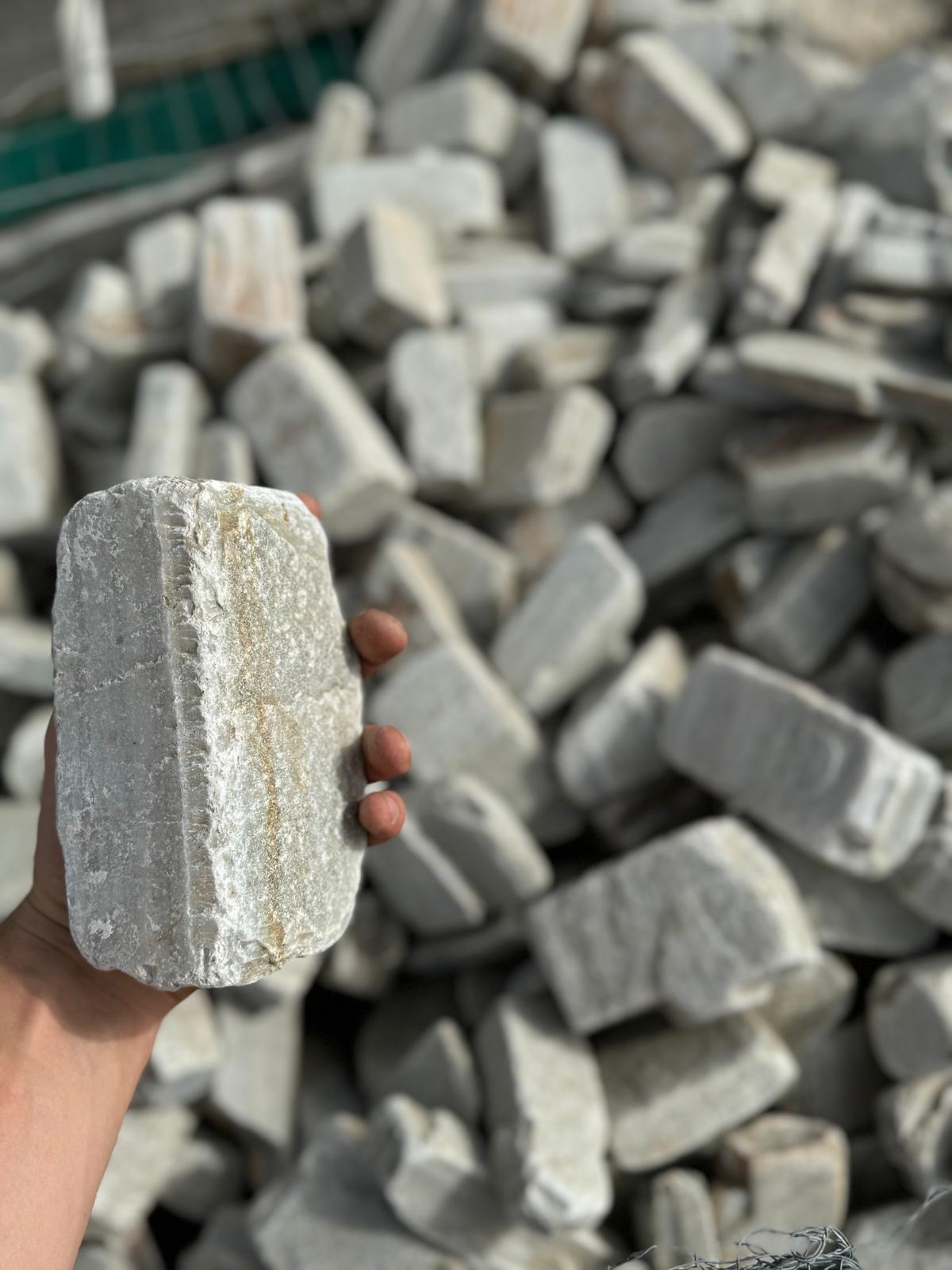 Hand holding a piece of limestone in front of a stockpile of landscape stone