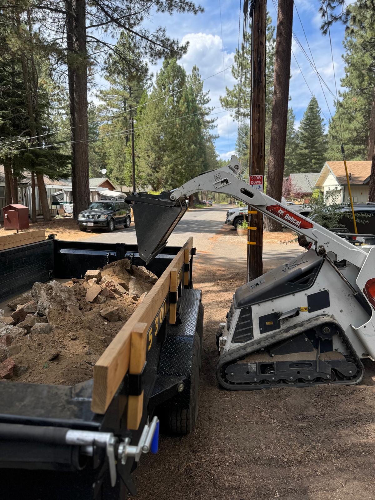 Bobcat MT100 mini skid steer loading rock into a dump trailer in a South Lake Tahoe backyard
