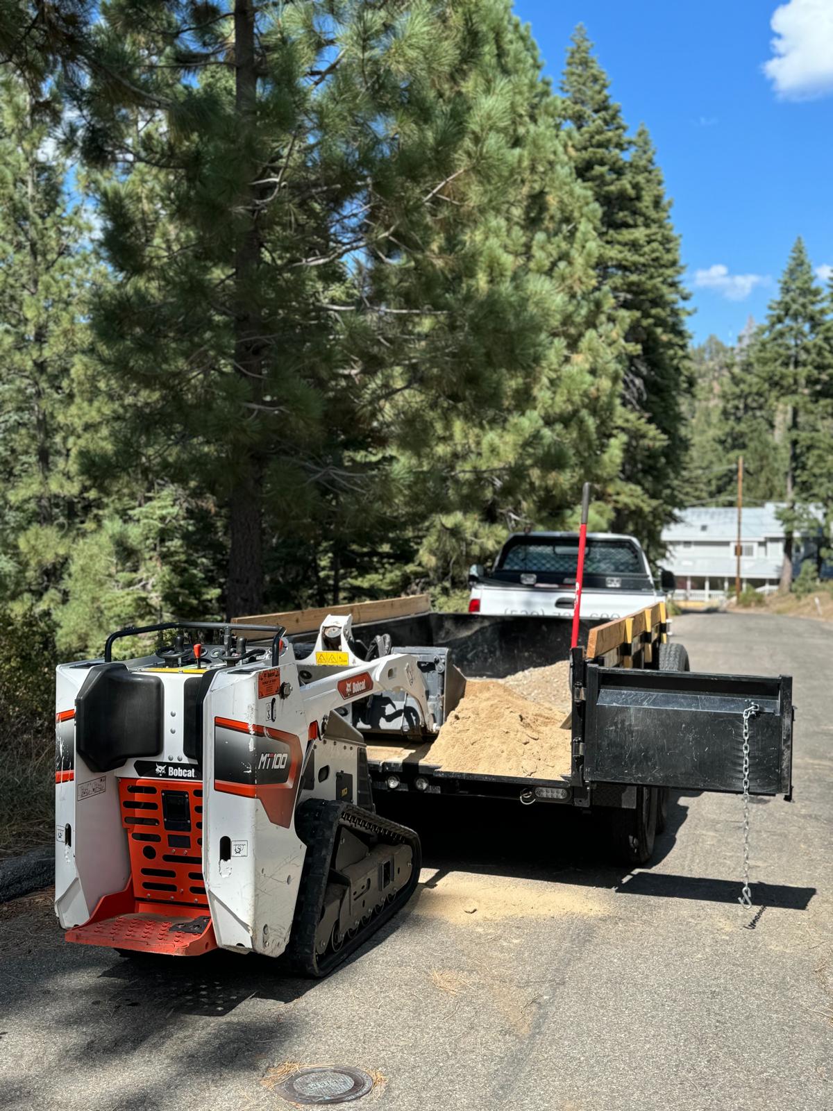 Bobcat MT100 mini skid steer beside a loaded dump trailer in South Lake Tahoe